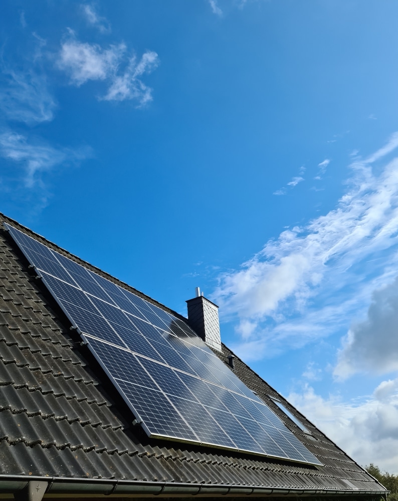 Panneaux solaires photovoltaïques sur un toit en tuiles noires sous un ciel bleu avec nuages légers.