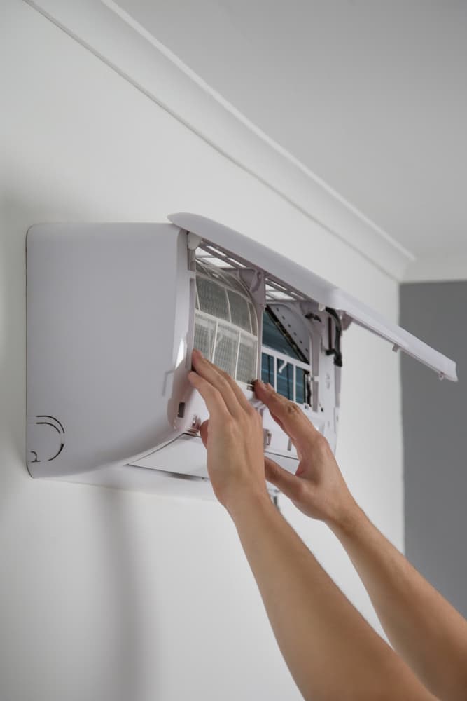 Entretien climatisation : Guide de nettoyage des filtres Mains retirant le filtre d'un climatiseur mural blanc pour un entretien régulier de l'appareil.
